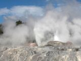 A dramatic geyser erupting with steam in a vibrant geothermal landscape.
