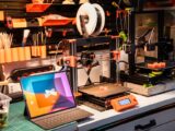 A high-tech workshop featuring 3D printers and a tablet on a desk, showcasing modern innovation.