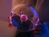 A woman holds a plasma ball emitting colorful electric arcs in a dimly lit room.