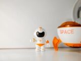 Close-up of a toy astronaut and space capsule on a white surface, ideal for children's play themes.
