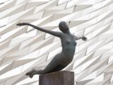 Stunning sculpture of a diving figure against the iconic Titanic Belfast architecture.
