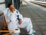 Man in astronaut costume sitting at an empty train station, evoking a sense of waiting and travel.
