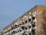 City apartment building with multiple balconies and satellite dishes under a clear sky.