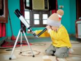 a little boy sitting on the floor looking through a telescope