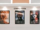 Framed posters of upcoming movies in a cinema hallway under 'Coming Soon' sign.