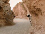 Astronauts peek from behind rocks in a fantasy extraterrestrial landscape.