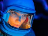 A close-up view of a woman in a spacesuit helmet illuminated by blue light, showcasing futuristic space exploration.