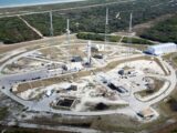 Drone view of spaceport with installed rocket ready for launching steel towers and hangar located amidst green forest