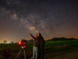 a man standing next to a telescope looking at the stars