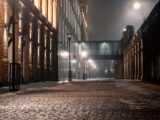 A foggy street with snow and illuminated buildings.