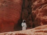 photography of astronaut standing beside rock formation during daytime