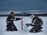 Two explorers use an ice auger on a frozen lake in Kiruna, Sweden during winter.