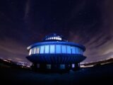 A UFO-shaped building lit up under a vibrant starry night sky in Karpacz, Poland.