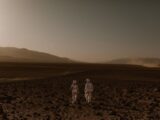 Two astronauts in spacesuits walk across a Mars-like desert landscape during the day.